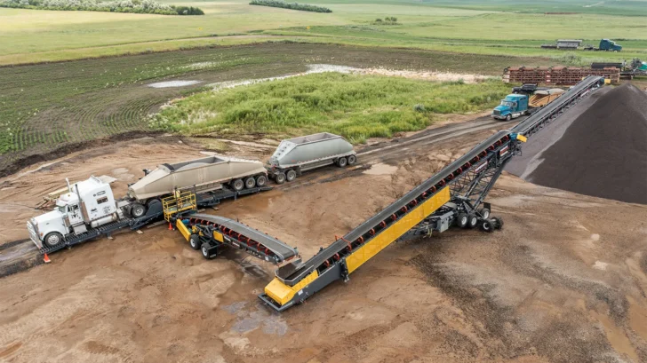 Truck Unloader receiving material from a dump truck and feeding a conveyor system with a wheel loader nearby.
